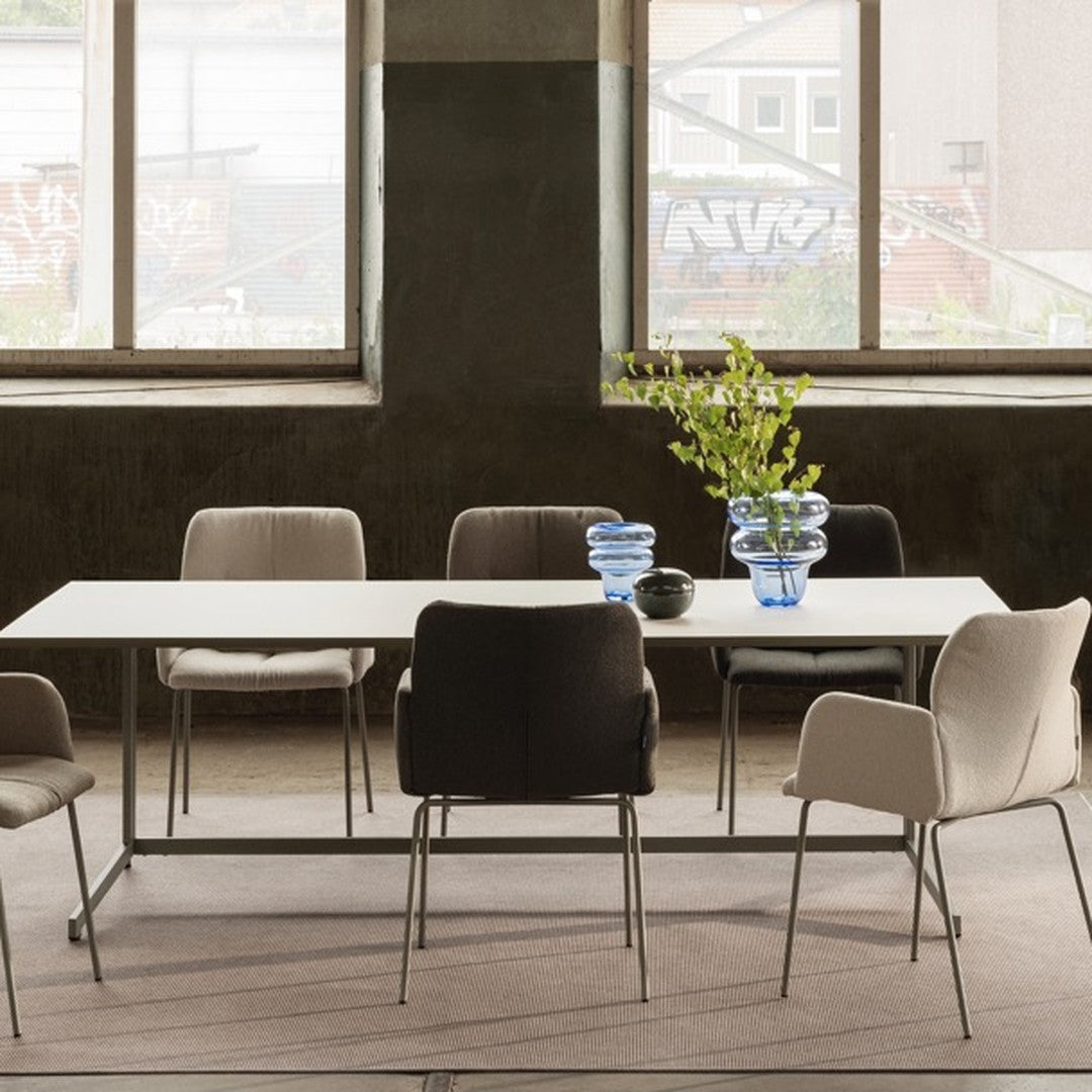Modern dining set featuring neutral-toned chairs in beige, gray, and black, with a sleek white table and blue glass vases.