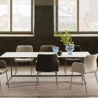 Modern dining set featuring neutral-toned chairs in beige, gray, and black, with a sleek white table and blue glass vases.