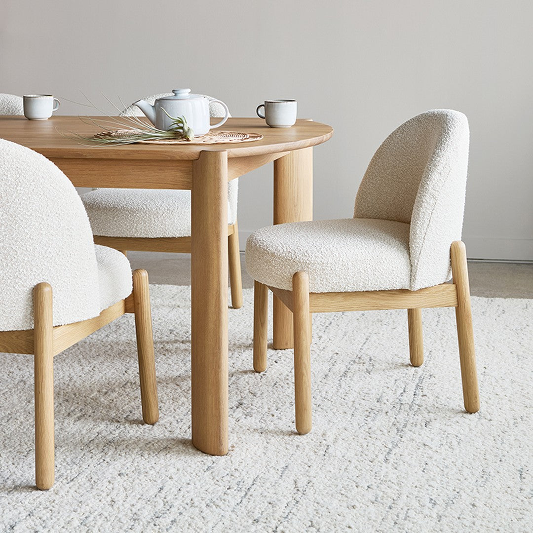 Light beige upholstered chairs with rounded backs, paired with a warm wooden table, set on a neutral-toned rug.