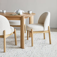 Light beige upholstered chairs with rounded backs, paired with a warm wooden table, set on a neutral-toned rug.