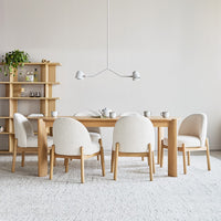 Light wood dining table with soft beige chairs on a neutral-toned rug. Minimalist and modern design elements.