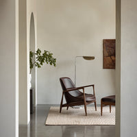 Mid-century modern brown leather chair on striped beige and white rug, surrounded by neutral-toned walls and decor.