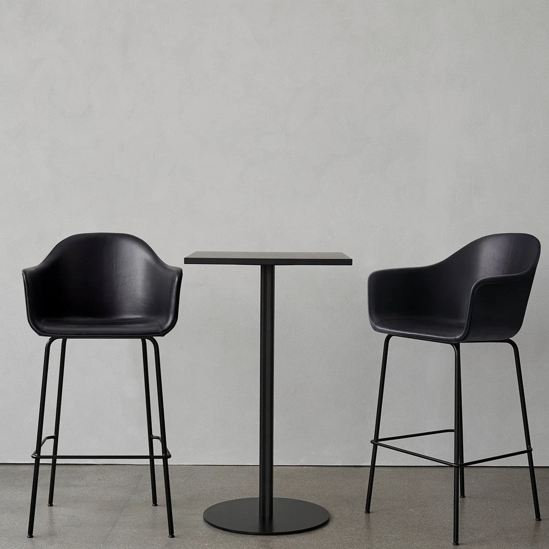 Modern black bar stools with sleek design paired with a minimalist black table on a concrete floor.