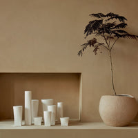 Assorted white ceramic vases with smooth finishes on a warm beige background, featuring simple, modern shapes.