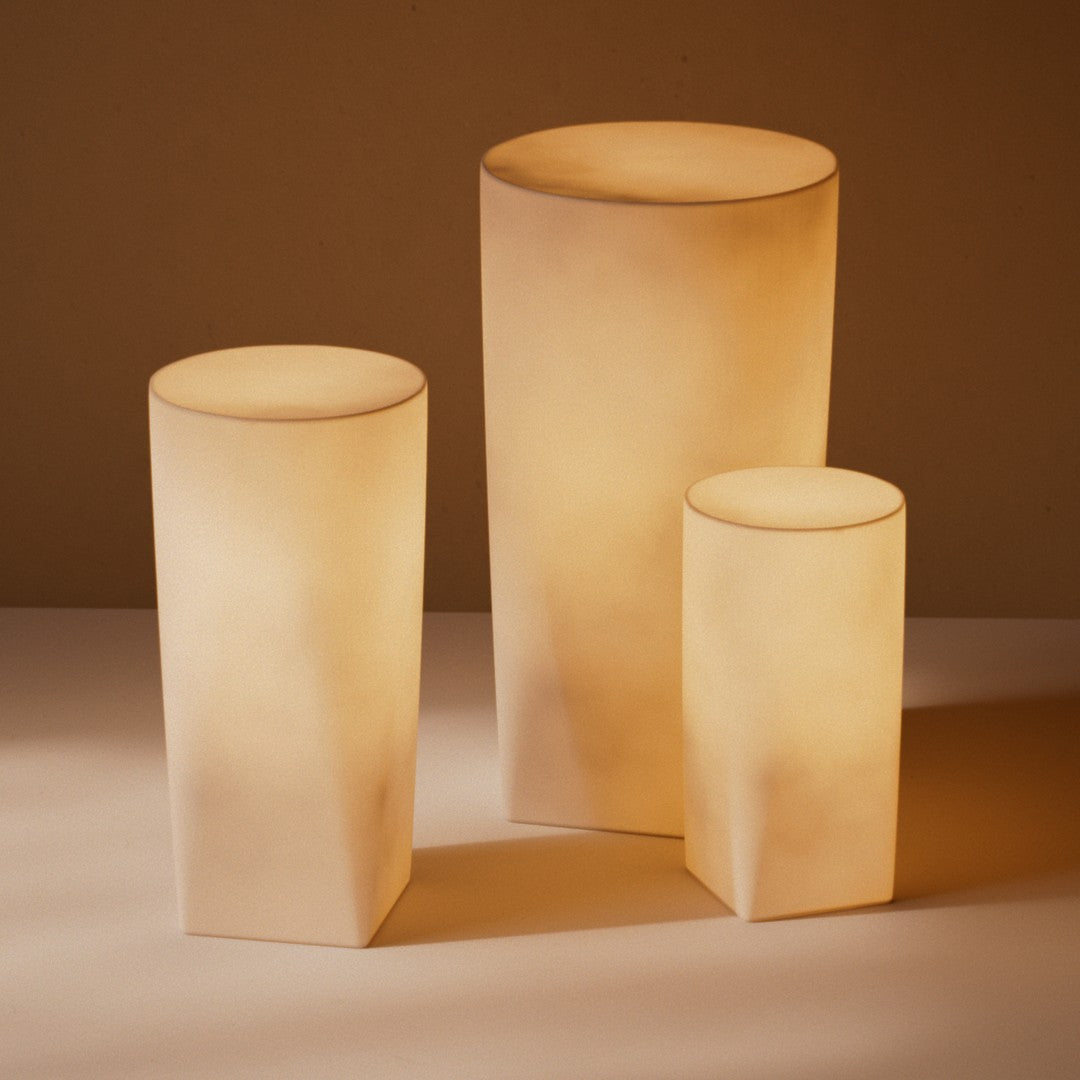 Three cylindrical lamps in soft beige tones with smooth, minimalist patterns, creating a warm ambient glow.