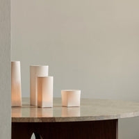 Soft white cylindrical lanterns on a marble table against a muted gray background, creating a calm, elegant ambiance.