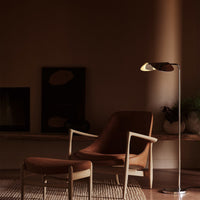 Elegant brown chair and ottoman with a sleek metallic floor lamp, set against a warm, muted backdrop.