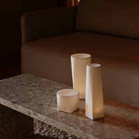 White geometric candles on a textured stone table, softly glowing against a brown couch backdrop.