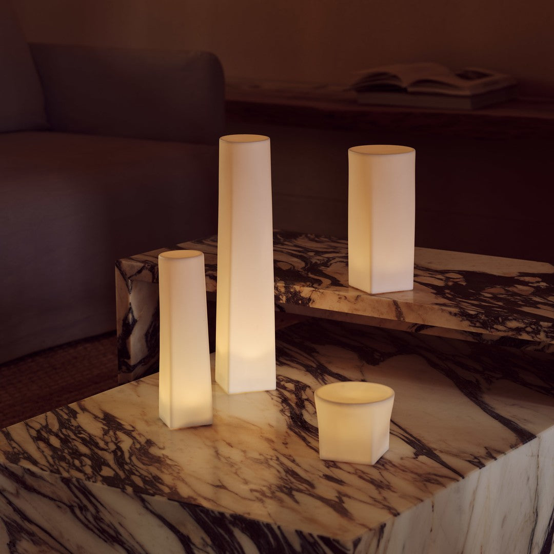 Warm white glow of geometric candle holders on a marble table with rich veining and soft, neutral tones.