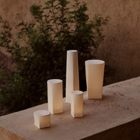 White geometric candle holders in various heights, showcasing soft, warm light against a natural background.