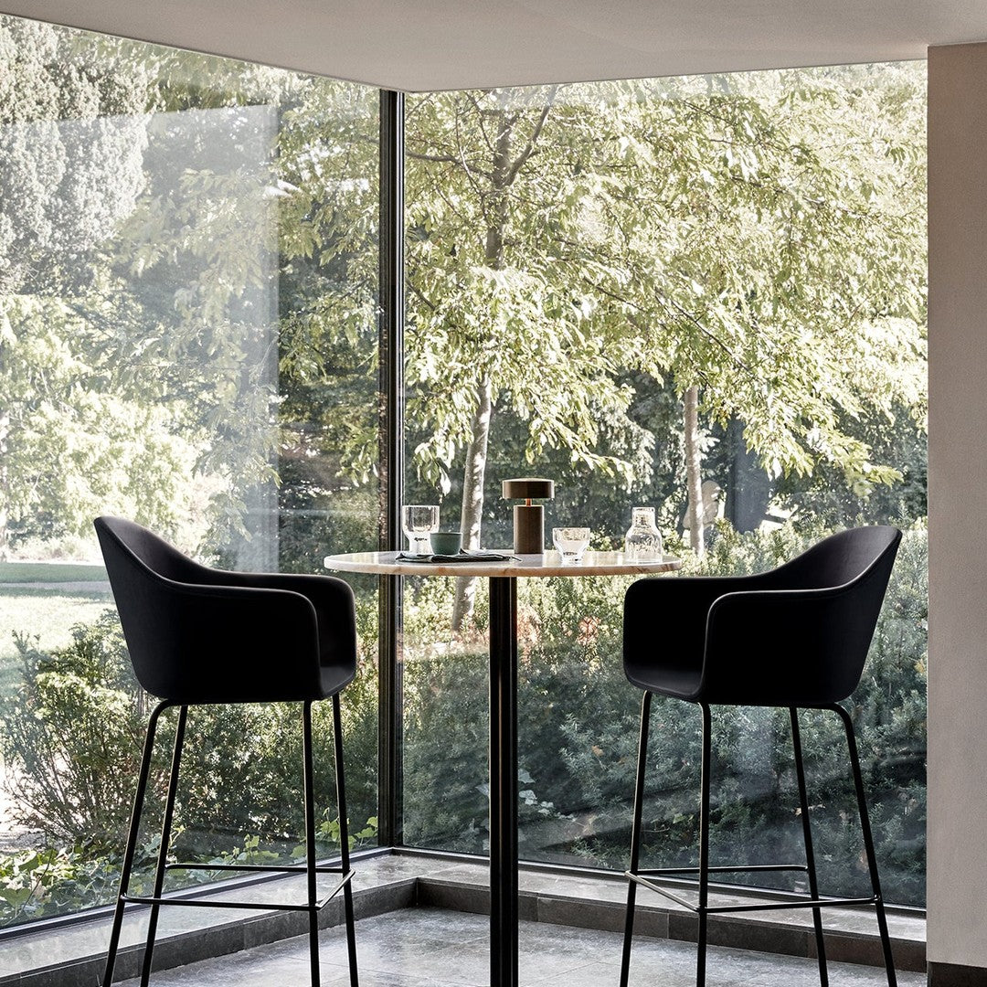 "Modern black bar stools paired with a sleek round table, set against a backdrop of lush green trees."