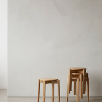Natural wood stools with a light honey tone, featuring a smooth, minimalistic design against a soft, neutral backdrop.