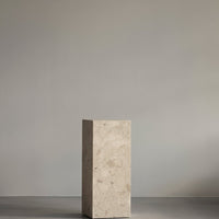 Neutral beige stone pedestal with subtle patterns, set against a soft gray background.