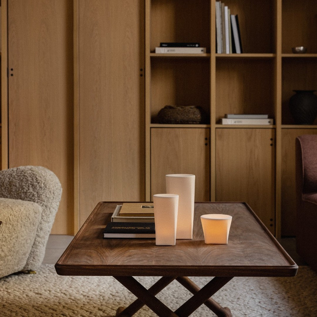 Wooden table with earthy tones, neutral candles, and soft textures in a cozy, minimalistic living space.