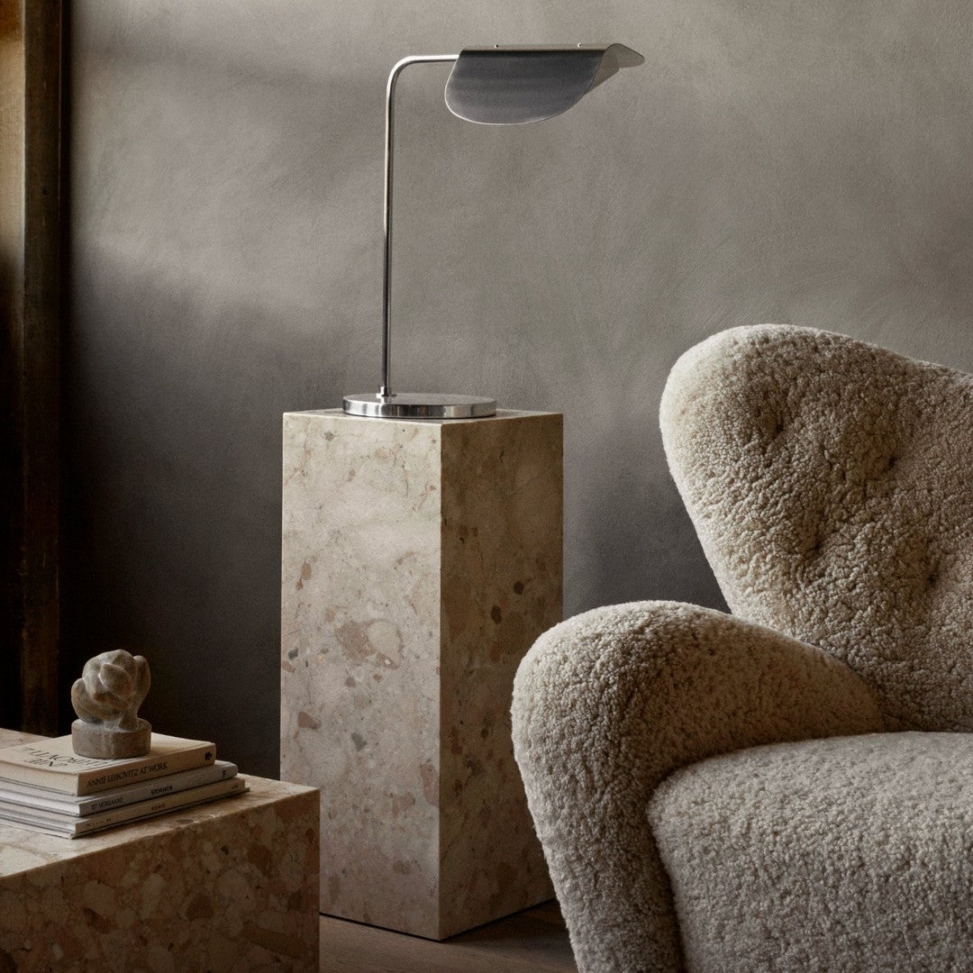 Stylish beige and cream textures on a soft armchair with a sleek metal lamp on a neutral pedestal. Modern home decor.