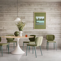 Dining area with a round table and green chairs against a wooden wall with a framed picture.