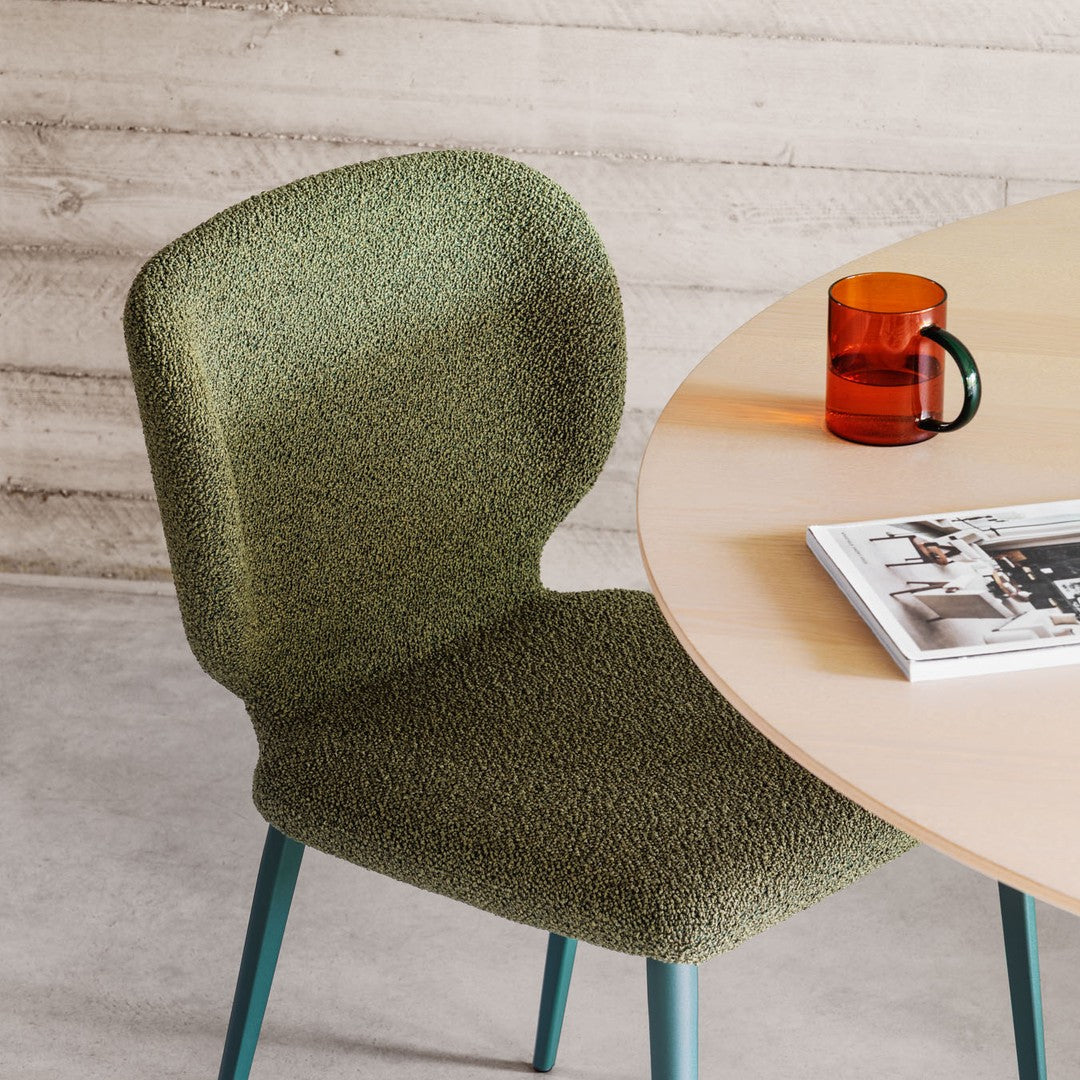 Green textured chair next to a round wooden table with a mug and magazine.