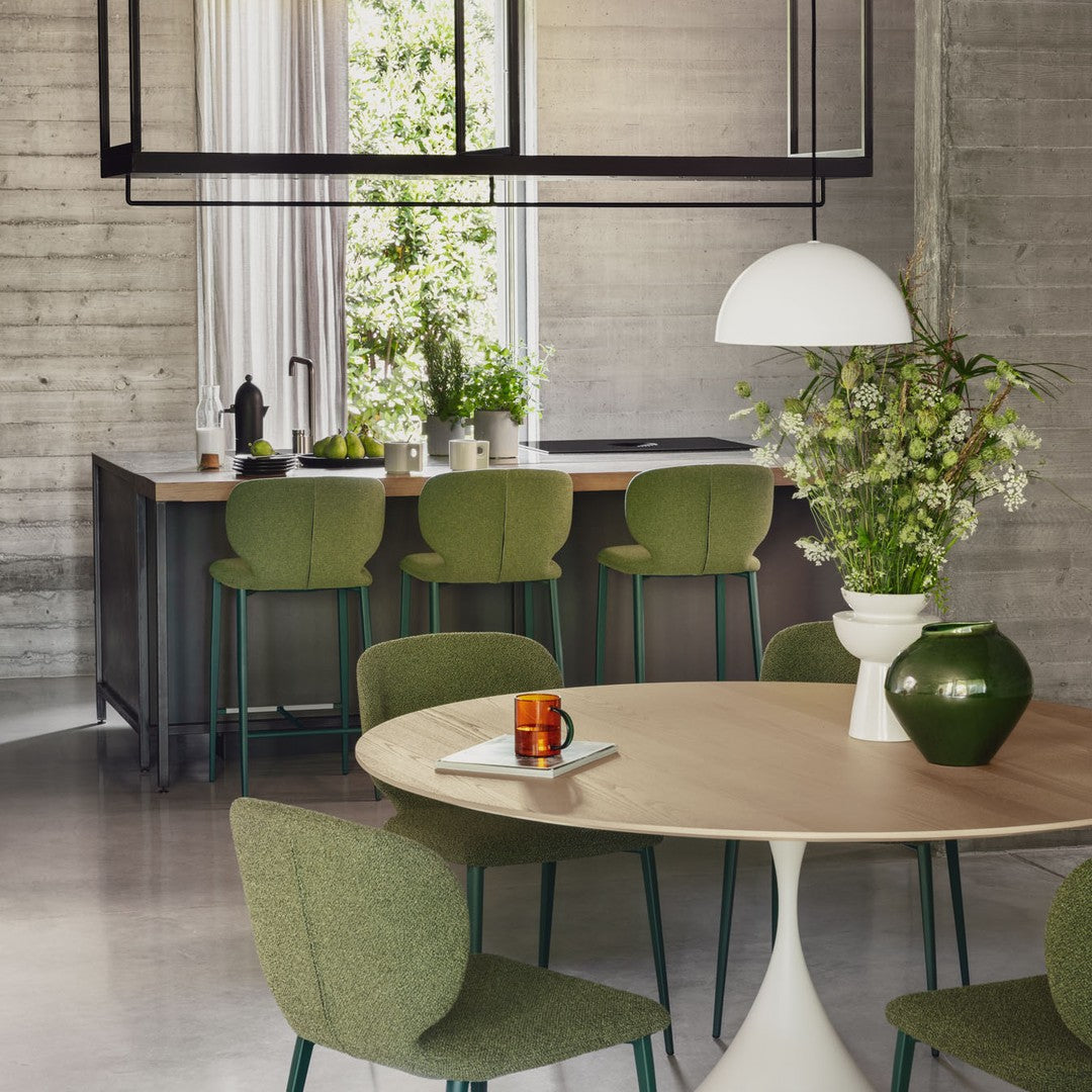 Modern kitchen with round wooden table and green chairs, featuring a vase of flowers and a cup.