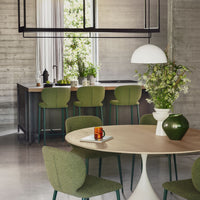 Modern kitchen with round wooden dining table and green chairs, featuring a vase of flowers and a cup.