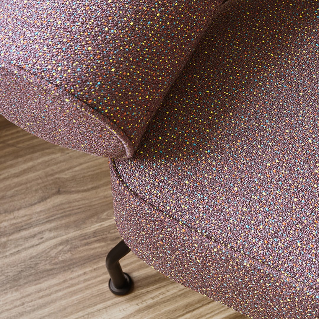 Close-up of a textured upholstery in light purple with multicolored speckles against a wooden floor.