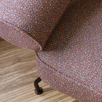 Close-up of a textured upholstery in light purple with multicolored speckles against a wooden floor.