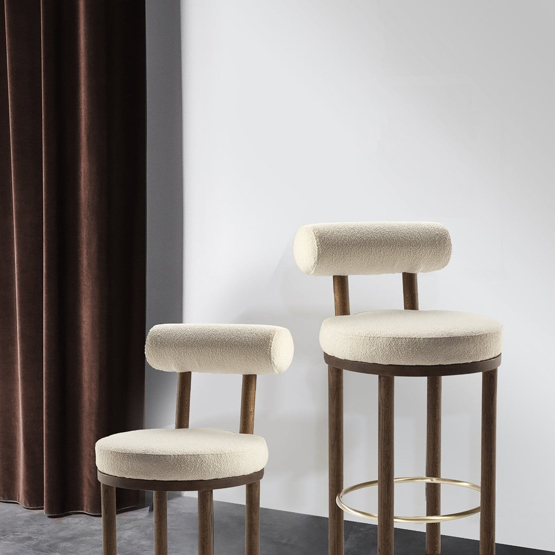 Beige upholstered bar stools with rounded backs, paired with warm wooden legs, against a dark velvet curtain backdrop.