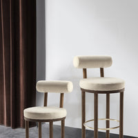 Beige upholstered bar stools with rounded backs, paired with warm wooden legs, against a dark velvet curtain backdrop.