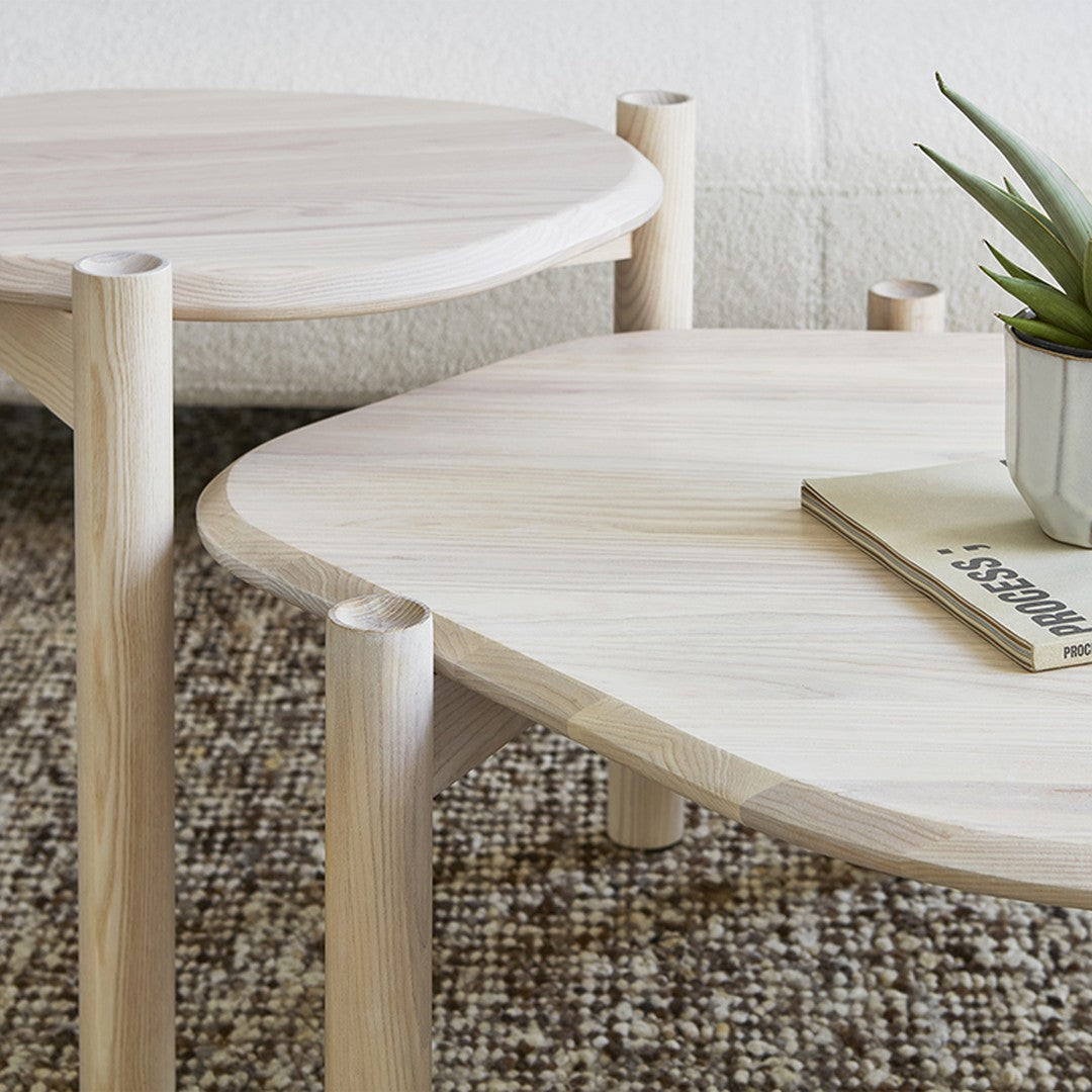 Light wood coffee tables with rounded edges and smooth surfaces, set atop a textured neutral patterned rug.