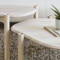 Light wood coffee tables with rounded edges and smooth surfaces, set atop a textured neutral patterned rug.