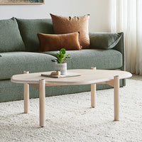 Natural wood coffee table with smooth, light finish, set against a soft green couch and cozy beige pillows.