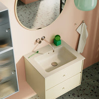 "Light yellow bathroom vanity with speckled countertop, pink walls, green accents, and a reflective round mirror."