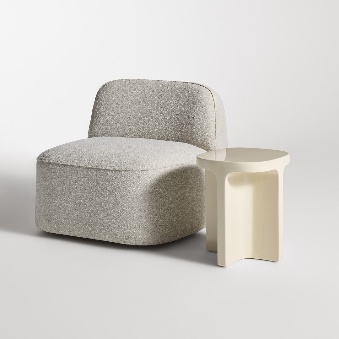 Light grey upholstered chair with soft, rounded edges next to a minimalistic cream side table.