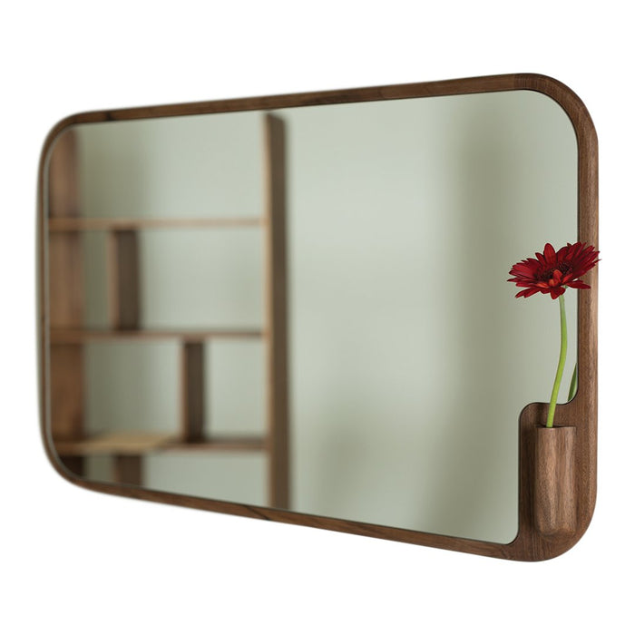 Wooden-framed mirror with a soft oval shape, featuring a light backdrop and a pop of red floral accent.