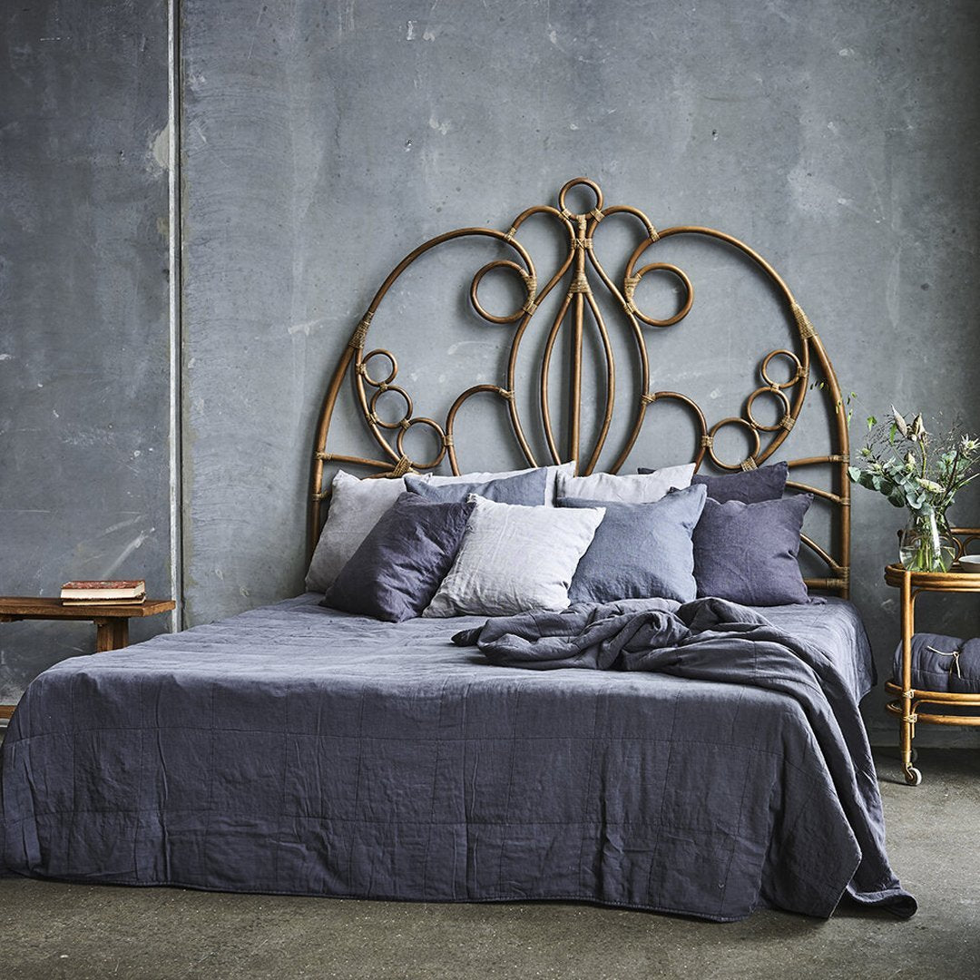 Metal headboard with intricate gold patterns atop a dark grey bedspread, accented by grey pillows and a natural-toned bedside table.