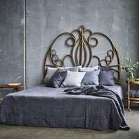 Metal headboard with intricate gold patterns atop a dark grey bedspread, accented by grey pillows and a natural-toned bedside table.