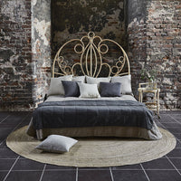 Elegant gray bedding set with decorative pillows, framed by a vintage wrought iron headboard and a natural fiber rug.