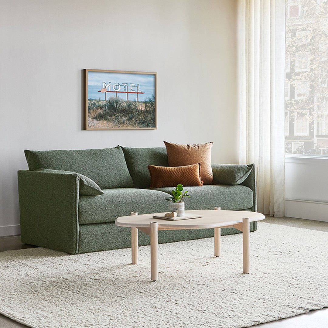 Green fabric sofa with rust-colored pillows, set on a beige rug, against a soft-lit neutral backdrop.