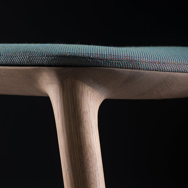 Close-up of a teal patterned seat on a wooden chair, showcasing intricate textures against a dark background.