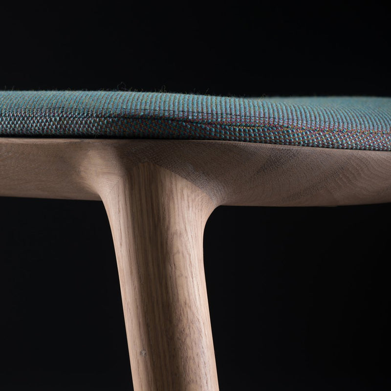 Close-up of a teal patterned seat on a wooden chair, showcasing intricate textures against a dark background.