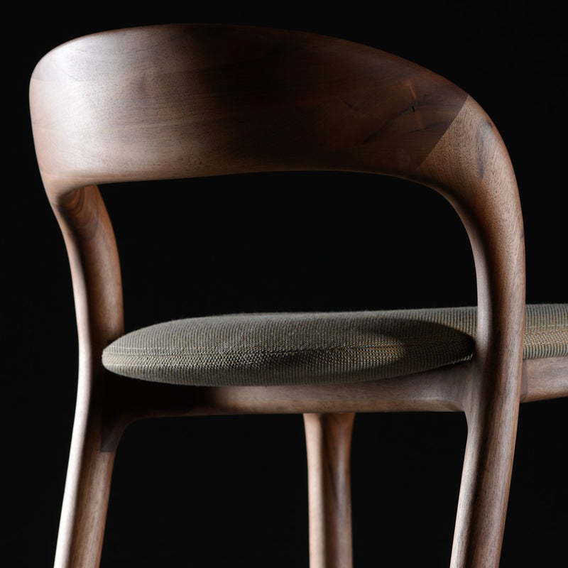 Dark wooden chair with a smooth finish and a beige woven seat, set against a black background.