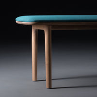 Turquoise upholstered bench with smooth wooden legs, showcasing a modern minimalist design and elegant curves.