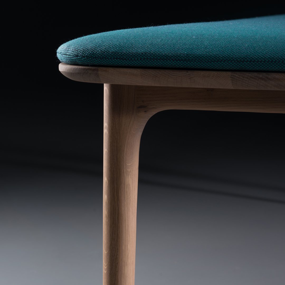 Teal cushioned seat with a smooth wood leg, showcasing a modern and minimalist design against a dark background.