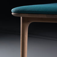 Teal cushioned seat with a smooth wood leg, showcasing a modern and minimalist design against a dark background.