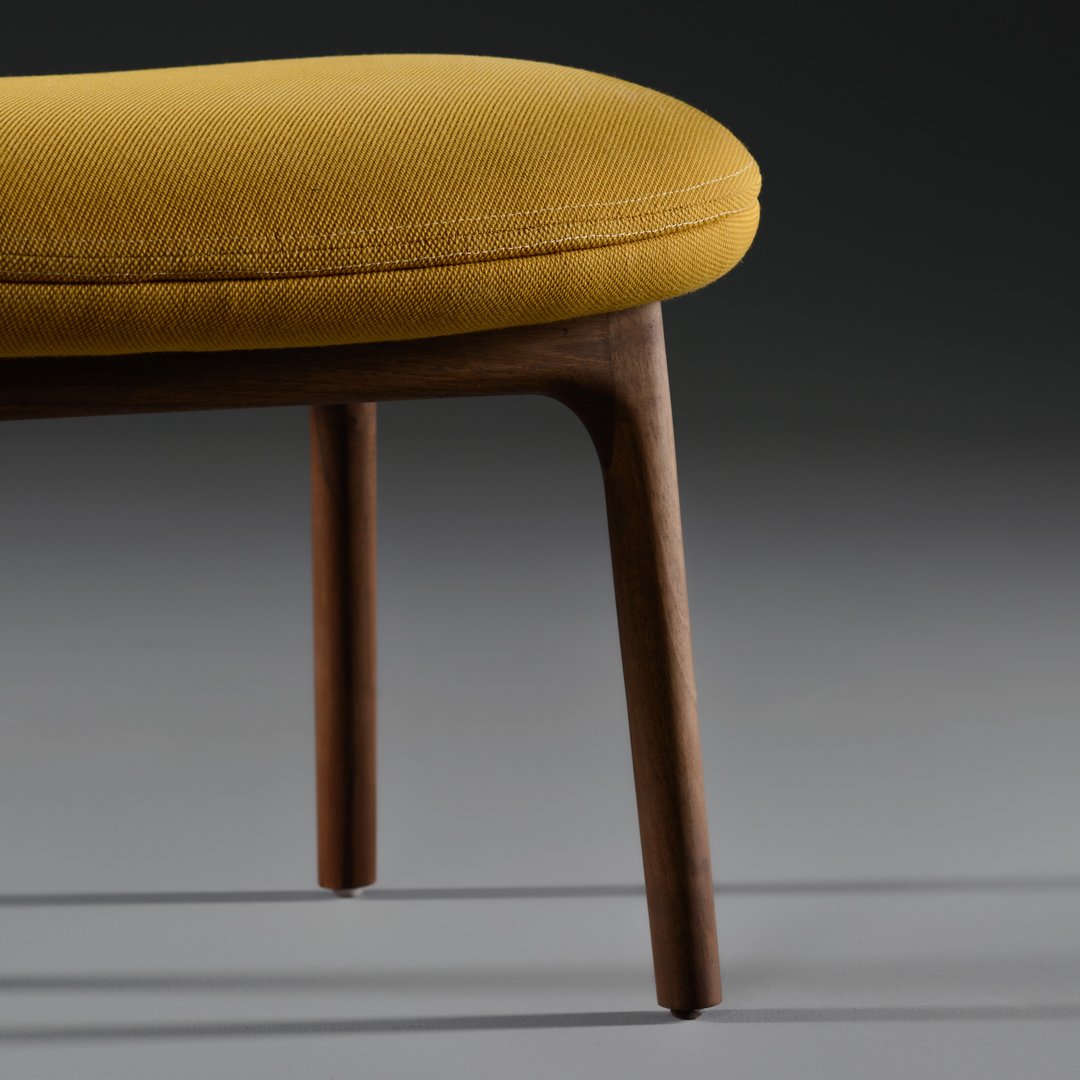 "Close-up of a mustard yellow upholstered seat with a textured finish and wooden legs."