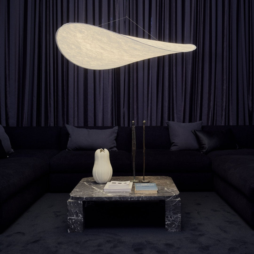 Elegant white pendant light above a dark sofa and marble coffee table, with rich navy curtains in the background.