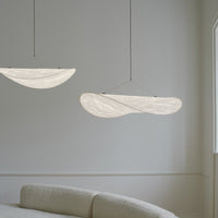 "Two soft white, curved pendant lights with a subtle, textured pattern, hanging elegantly in a minimalist interior."