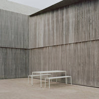 Modern white tables against a textured gray wooden wall, enhancing contemporary minimalist design.