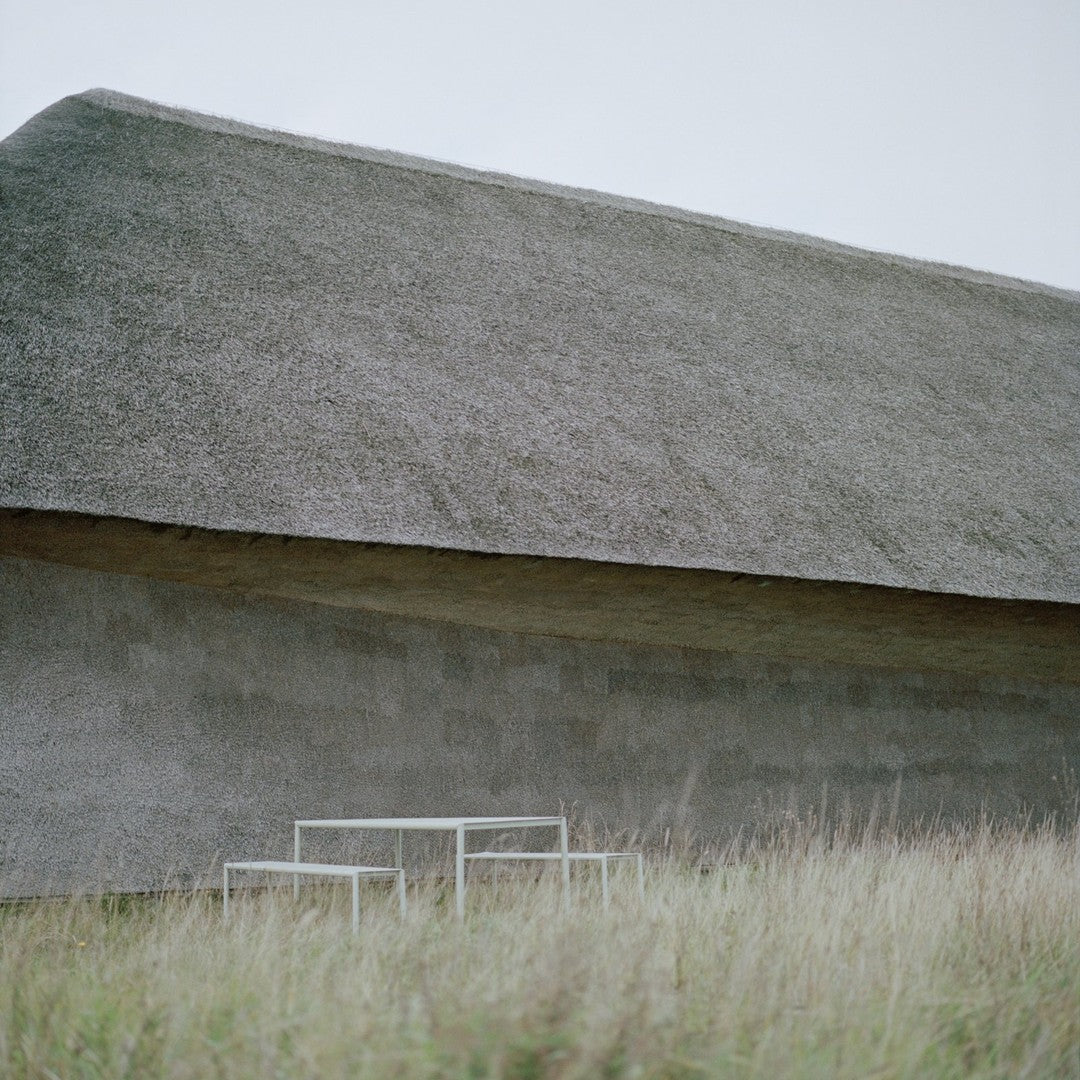 Grey thatched roof on a minimalist building with a textured stone wall, surrounded by green grass.