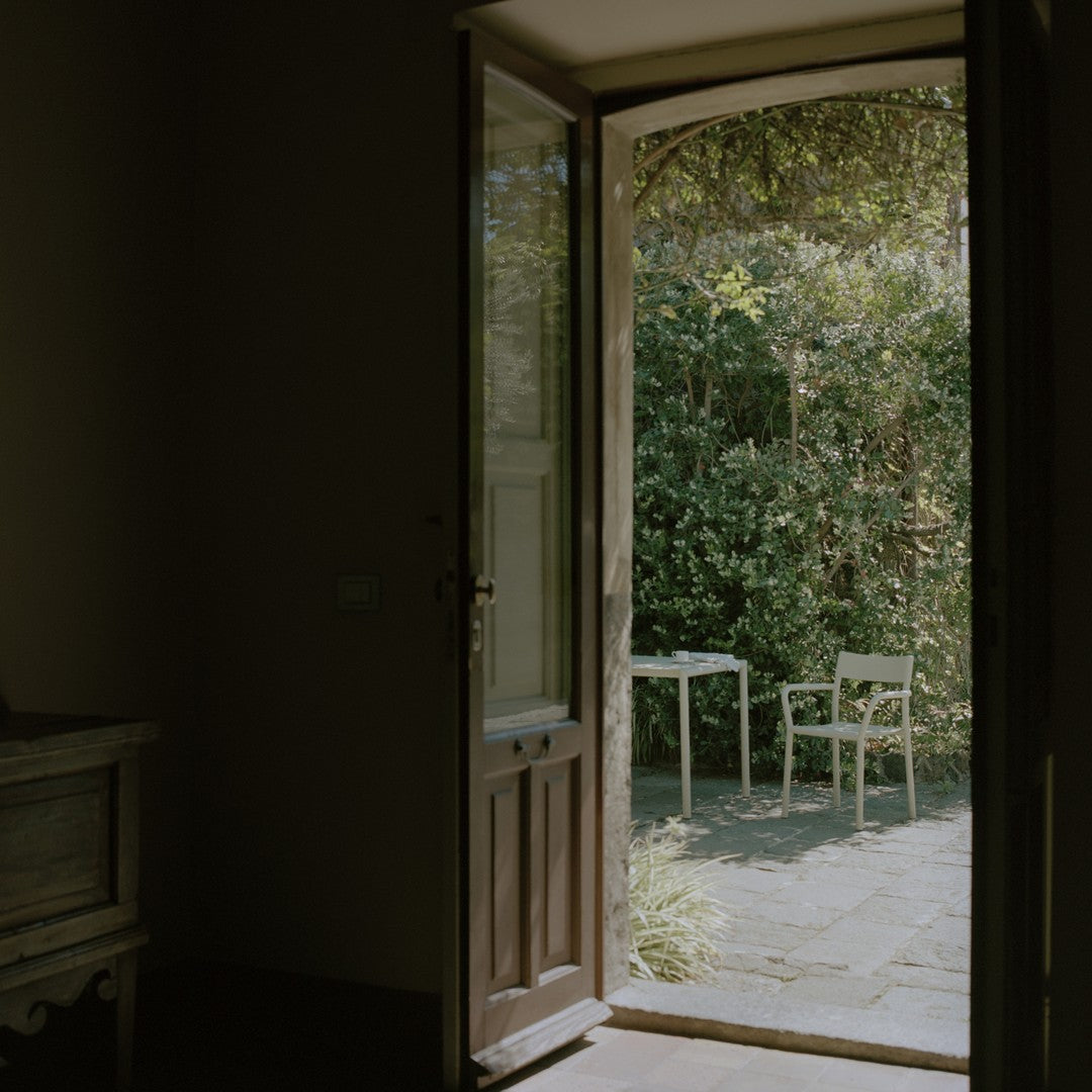 "Natural light pours through an open wooden door into a sunlit green garden with subtle stone patterns."