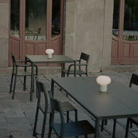 Black metal outdoor dining table with simple design, paired with sleek black chairs and a white glowing lamp centerpiece.